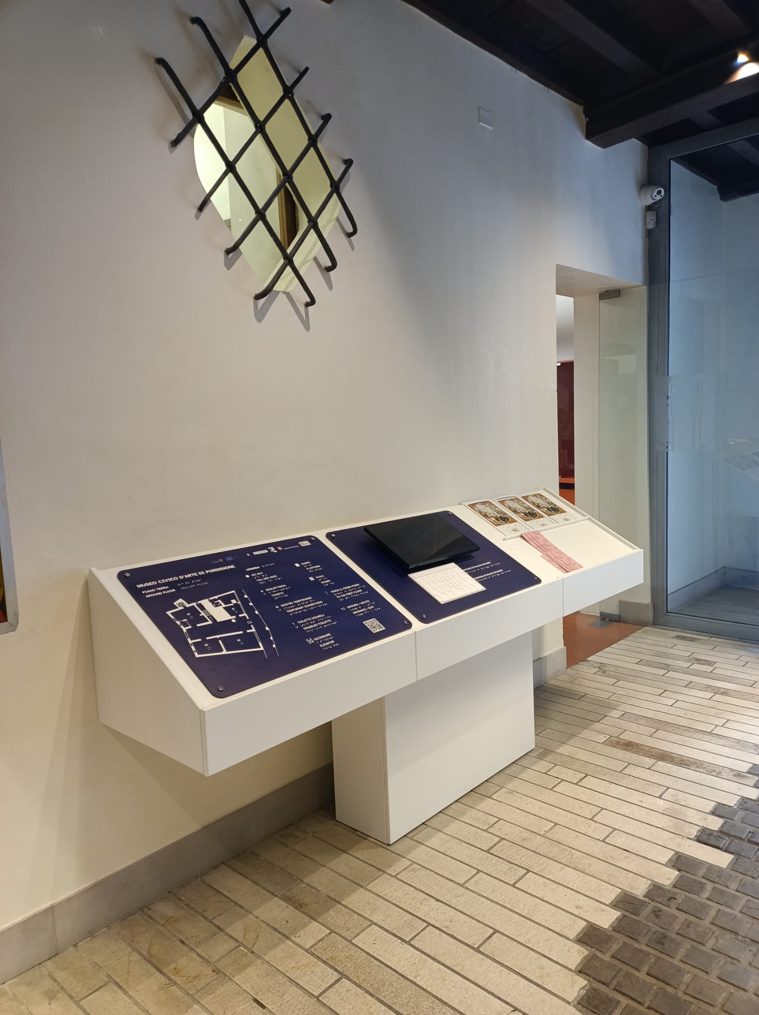 Tavolo introduttivo del museo con mappa tattile e rilievo della facciata di Palazzo Ricchieri; uno schermo trasmette video bilingue sottotitolati per l'orientamento narrativo dei visitatori.